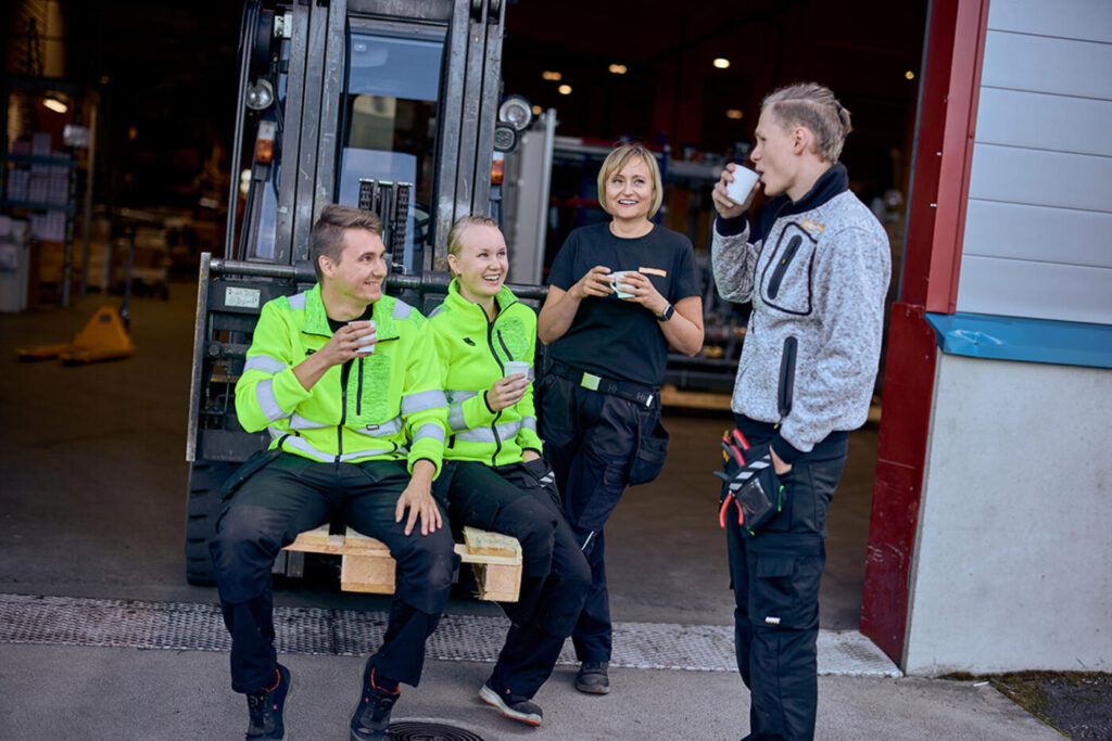 Kolme hymyilevää huoltohenkilöä huomiovaatteissa